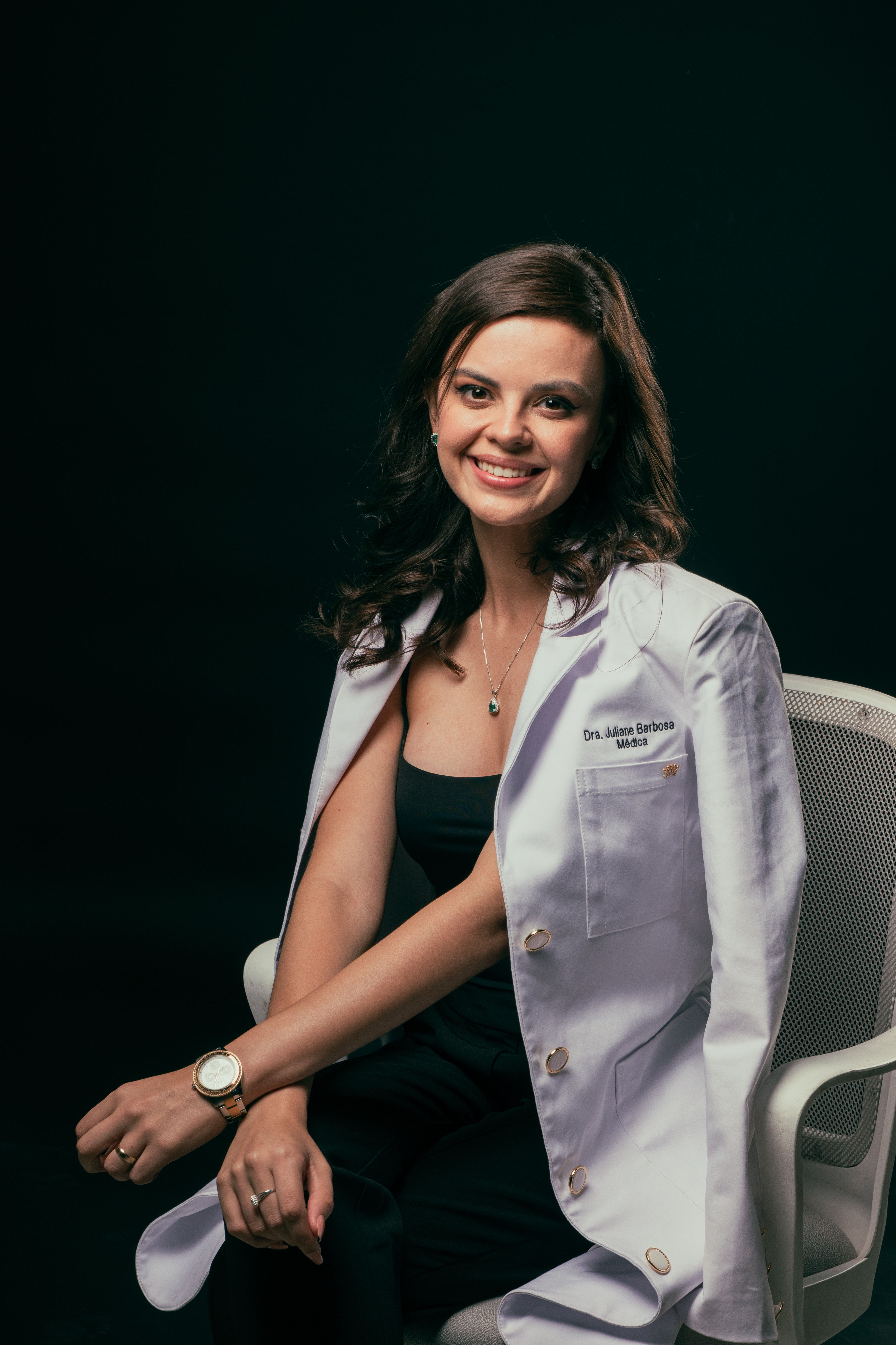 Dra. Juliane Barbosa, sentada e sorrindo, com jaleco branco