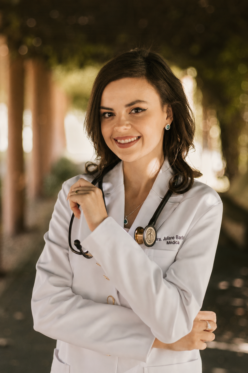 Dra. Juliane Barbosa sorrindo, de jaleco branco, em ambiente externo